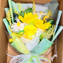 Bouquet of yellow flowers with greenery in a clear plastic wrap on a brown background